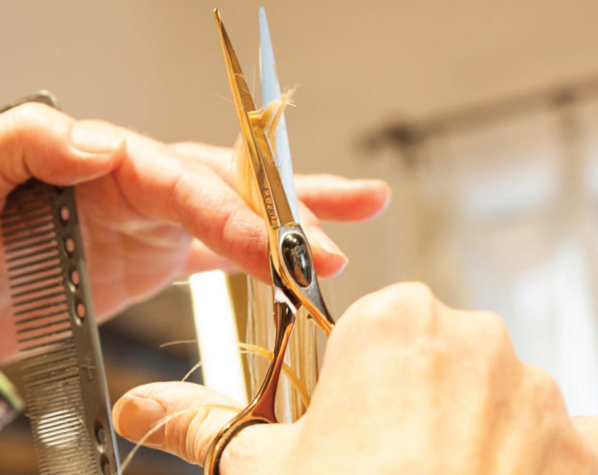 Close-up of a hairstylist's hands skillfully cutting hair with scissors and holding a comb, focusing on the precision of the haircut.