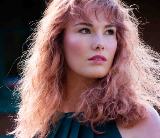 Woman with voluminous, curly pink hair looking contemplatively to the side