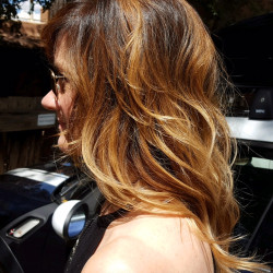 Woman with medium-length hair featuring a balayage coloring from deep brown roots to honey blonde ends, styled in soft waves
