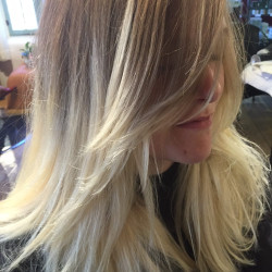 Woman with long blonde hair featuring dark roots, styled in smooth layers with face-framing highlights
